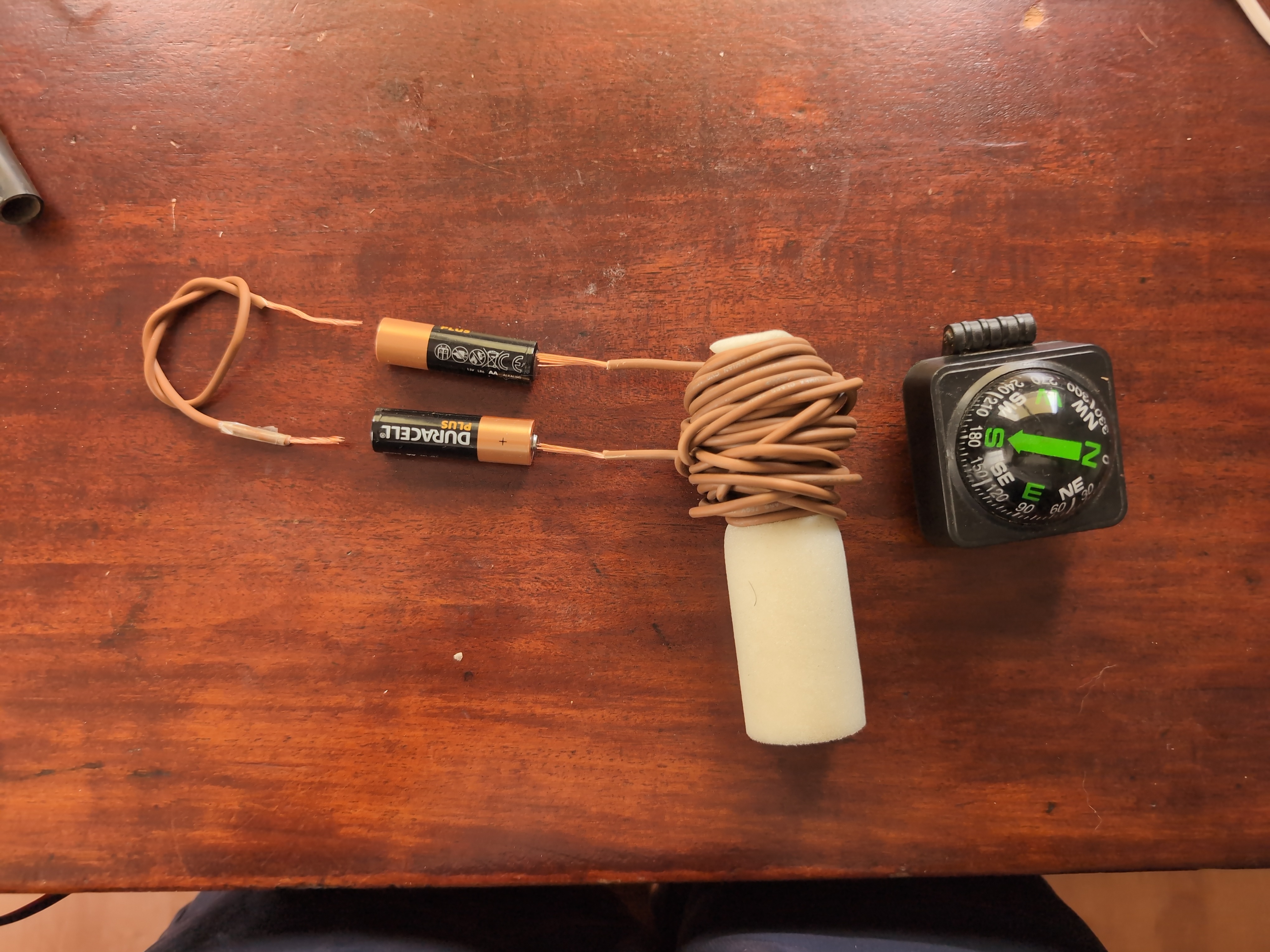 Foto aèria de l'electroiman sobre la taula de la meva habitació. L'electroiman està format per un cable enrotllat al voltant d'un corro i dues piles connectades en un circuit sense resitència. Al costat s'hi veu una brujola